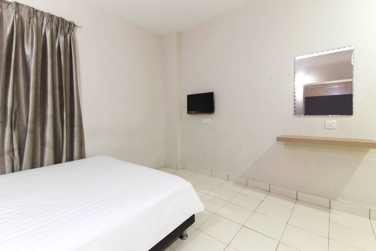 A bedroom with a bed, a television, a mirror, and a shelf.