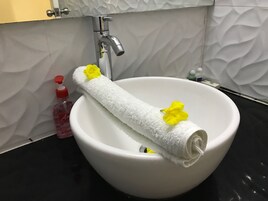 A white basin with a rolled towel and yellow flowers, a red soap dispenser, and a silver faucet in a bathroom.