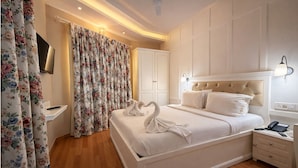 Une chambre d’hôtel avec un grand lit, une table de chevet avec une lampe, un téléviseur à écran plat et des rideaux à motifs floraux.