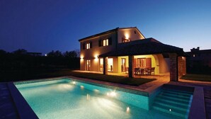 Une maison à deux étages avec une piscine, du mobilier d’extérieur et une structure en pierre.