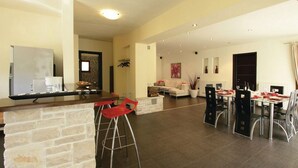 A spacious living area with a dining table set for four, a kitchen area with a bar, and a cozy seating area with a sofa and chairs. - Luxury villa with heated pool and large private garden, near the sea (Peroj)