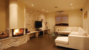 A cozy living room with a stone fireplace, a flat-screen TV, a white sofa, and a glass coffee table. - Luxury villa with heated pool and large private garden, near the sea (Peroj)