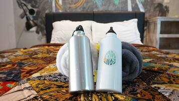 A bed with a patterned bedspread, two water bottles, and a rolled towel.