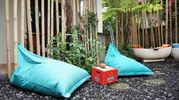 A garden area with two turquoise cushions, a red Bintang Pilsener box, and a white bathtub.
