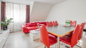 Een moderne woonkamer met een rode bank, een eettafel met rode stoelen en een potplant.