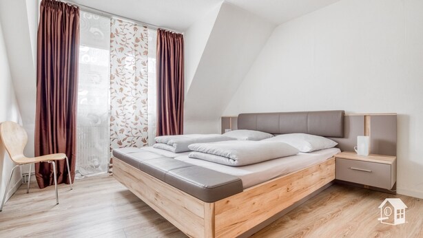 Een moderne slaapkamer met een houten bed, een nachtkastje, een stoel en een raam met gordijnen.