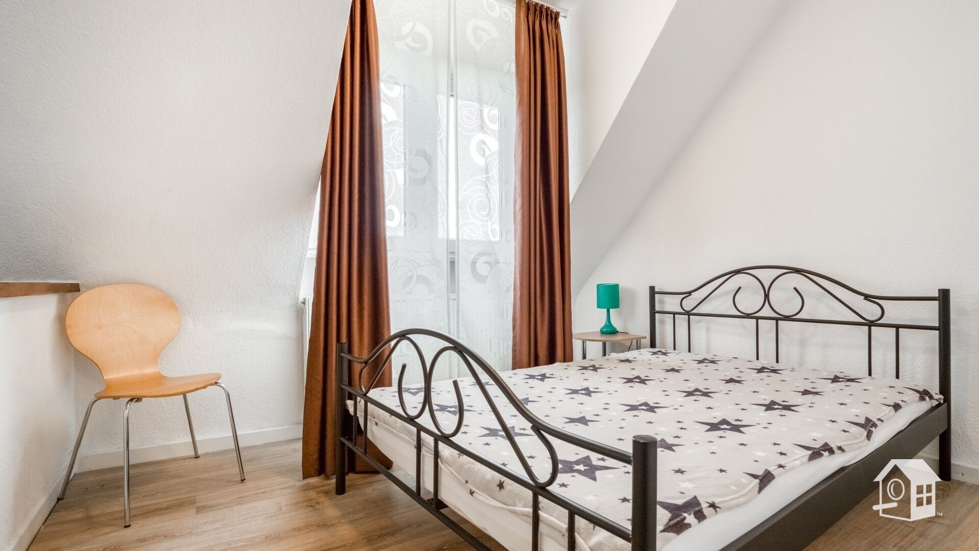 Ein Schlafzimmer mit Bett, Stuhl, Nachttisch und einem Fenster mit Vorhängen.