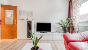 Een moderne woonkamer met een flatscreen televisie, een rode bank, een salontafel met een plant en een houten deur met prikbord.