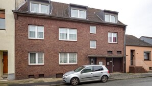Een twee verdiepingen tellend bakstenen gebouw met meerdere ramen, een auto voor de gevel en zichtbaar nummer 68.