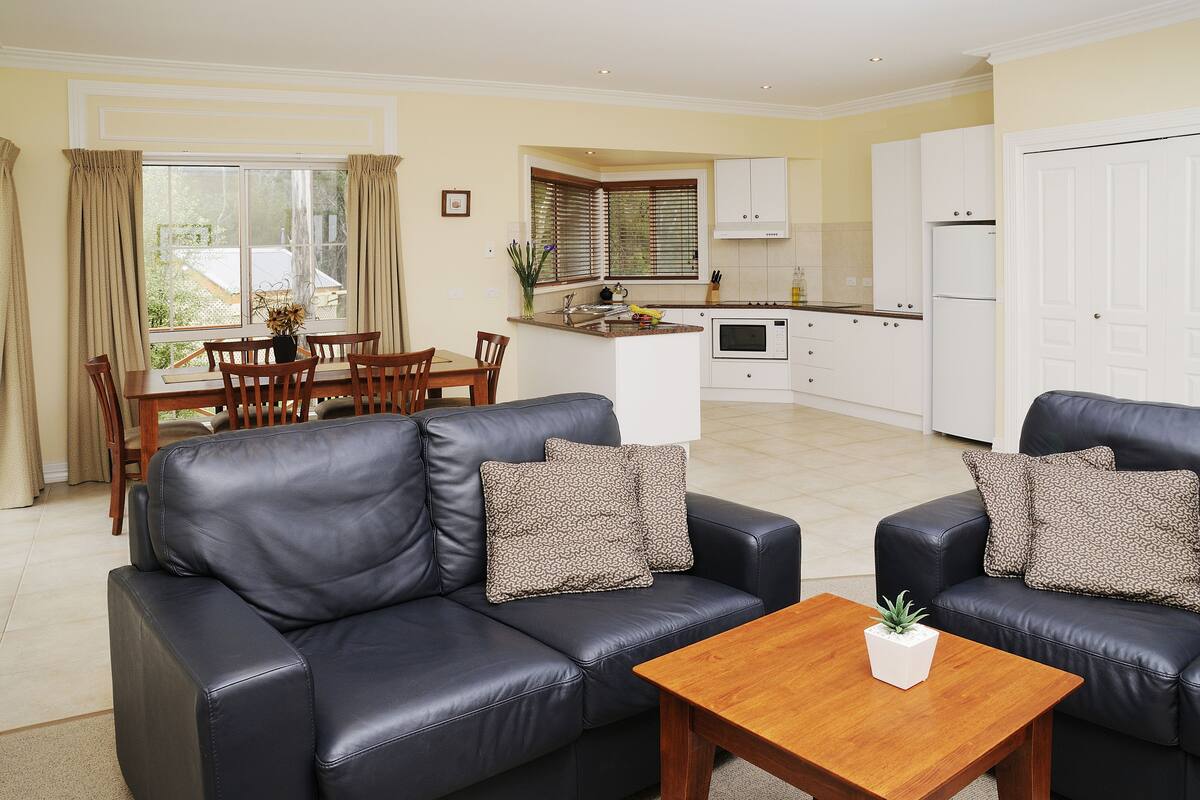 Una sala de estar moderna con un sofá de cuero negro, una mesa de centro de madera y un comedor con mesa y sillas.