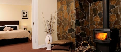 A bedroom with a stone fireplace, a bed, a vase with branches, and a door leading to another room.