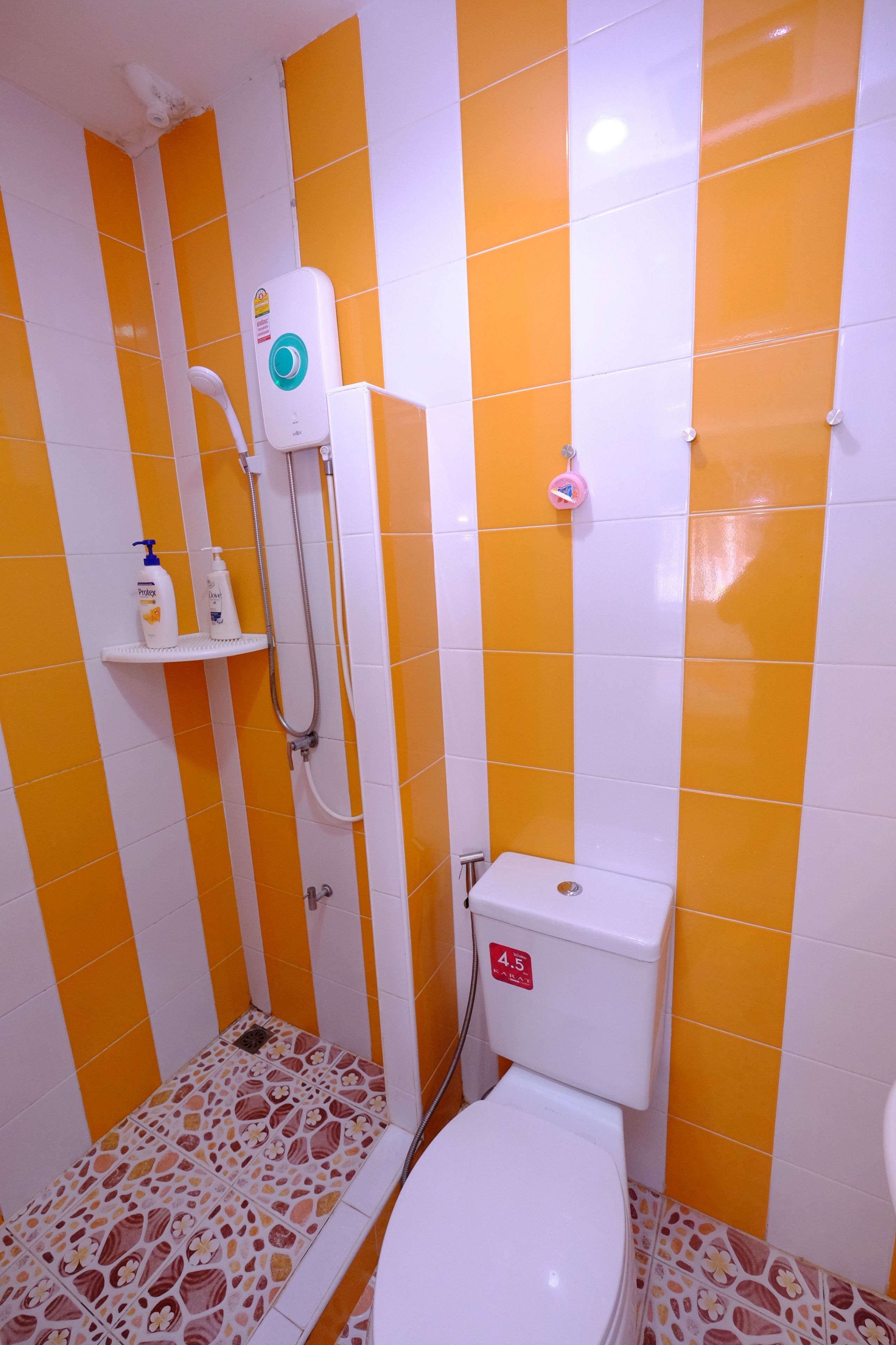 Kylpyhuoneessa on oranssit ja valkoiset laatat, wc, suihku ja hylly, jossa on hygieniatuotteita.