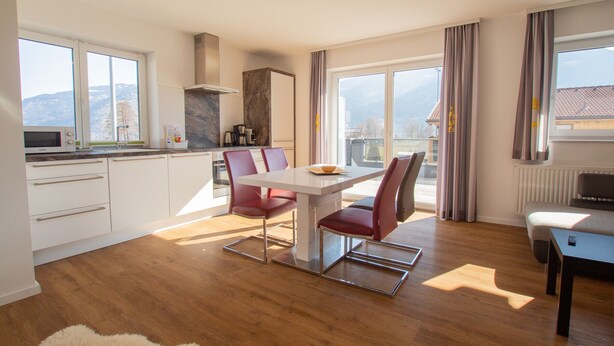A modern kitchen with white cabinets, a microwave, and a coffee machine. There is a dining table with red chairs and a view of mountains through large windows. - Panorama App 2A am See, für max.4,free WIFI (Zell am See)