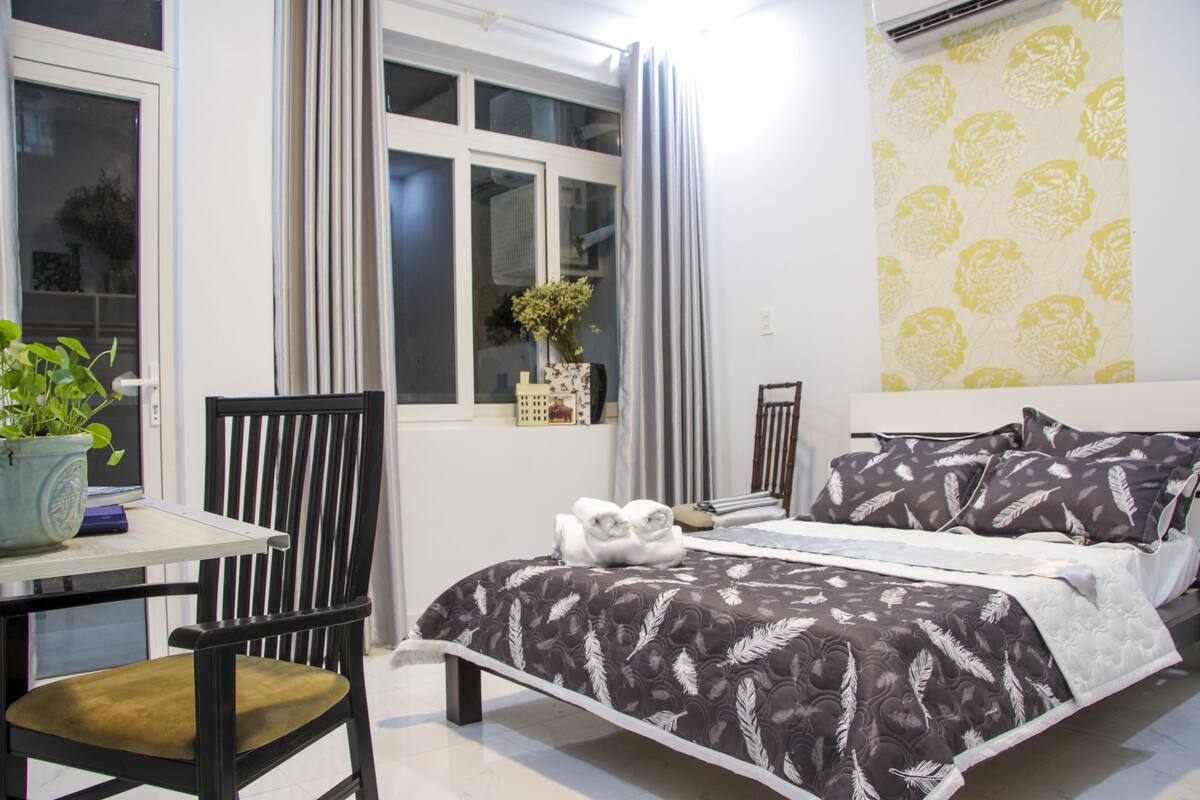 A bedroom with a bed, a chair, a table, and a window with curtains.