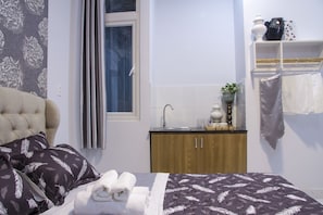 A neatly arranged bedroom with a bed, pillows, a bedside table with a lamp, a small cabinet, and a window with curtains.