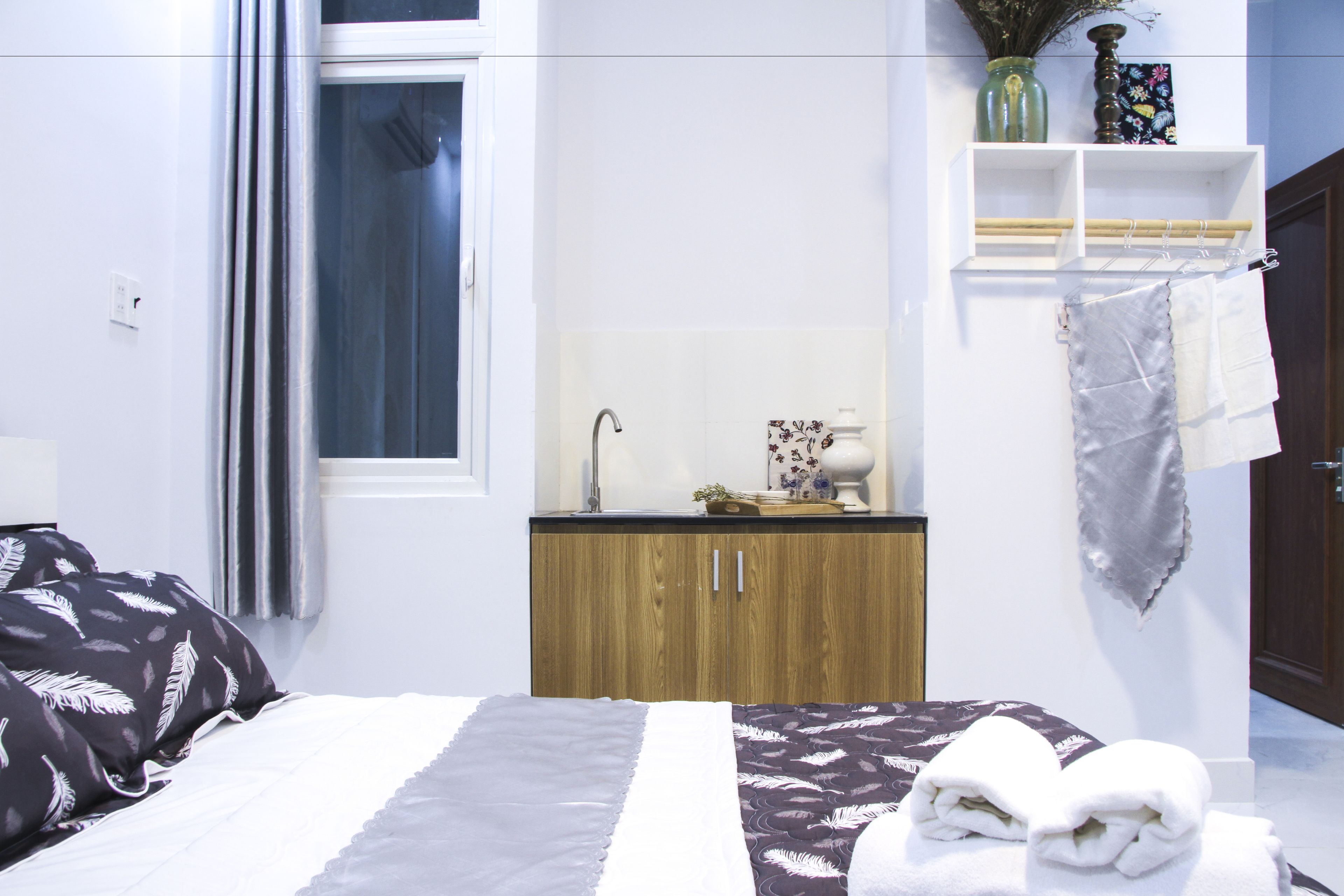 A hotel room with a bed, a wooden cabinet, a sink, and a shelf with towels.
