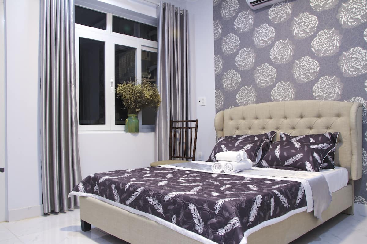 A neatly made bed with a patterned bedspread, a tufted headboard, and a window with curtains.