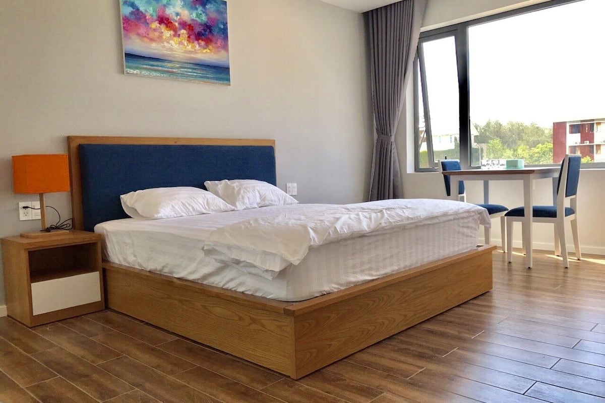 Cama bem arrumada com lençóis brancos em quarto com piso de madeira e uma janela grande.