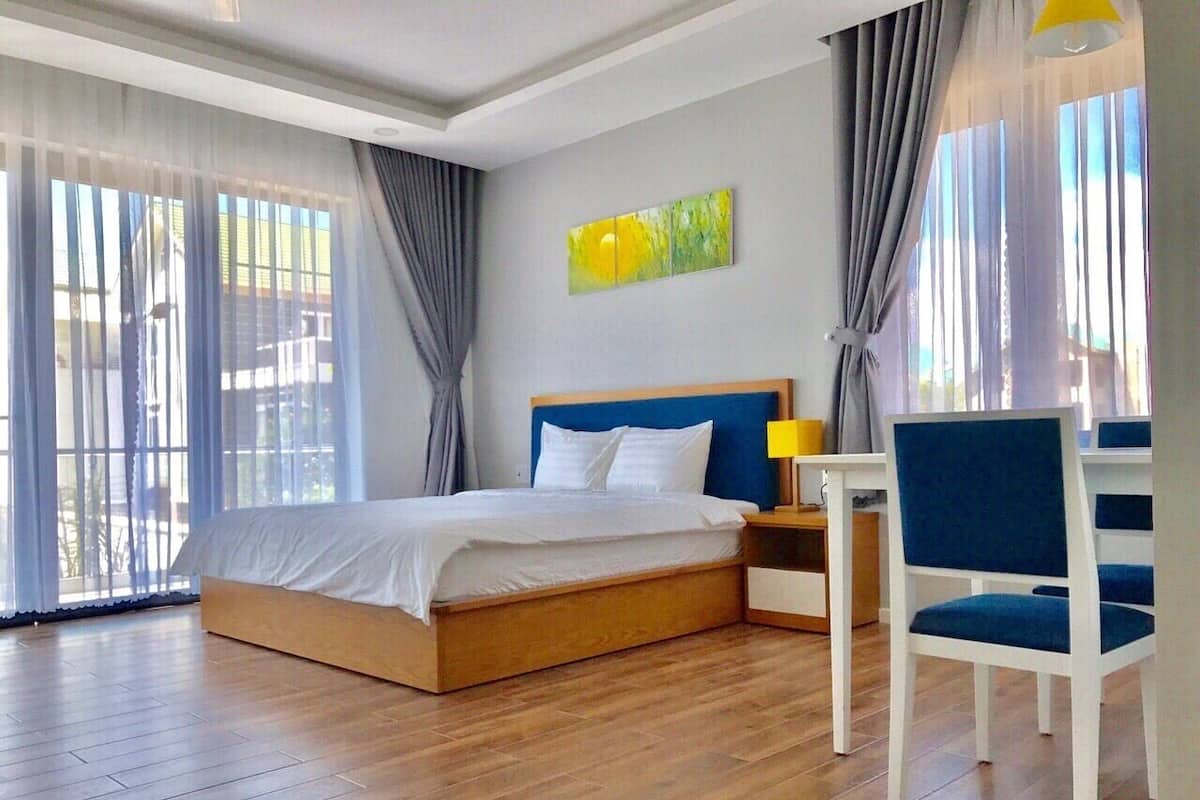 Um quarto moderno com cama de madeira, cabeceira azul, mesa de cabeceira branca, cadeira azul e abajur amarelo.