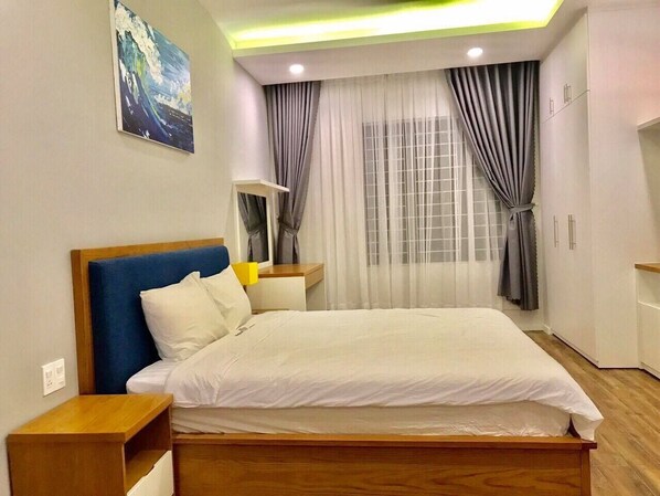 Una habitación de hotel moderna con una cama grande, cabecero de madera, una mesita de noche y un ventanal con cortinas.