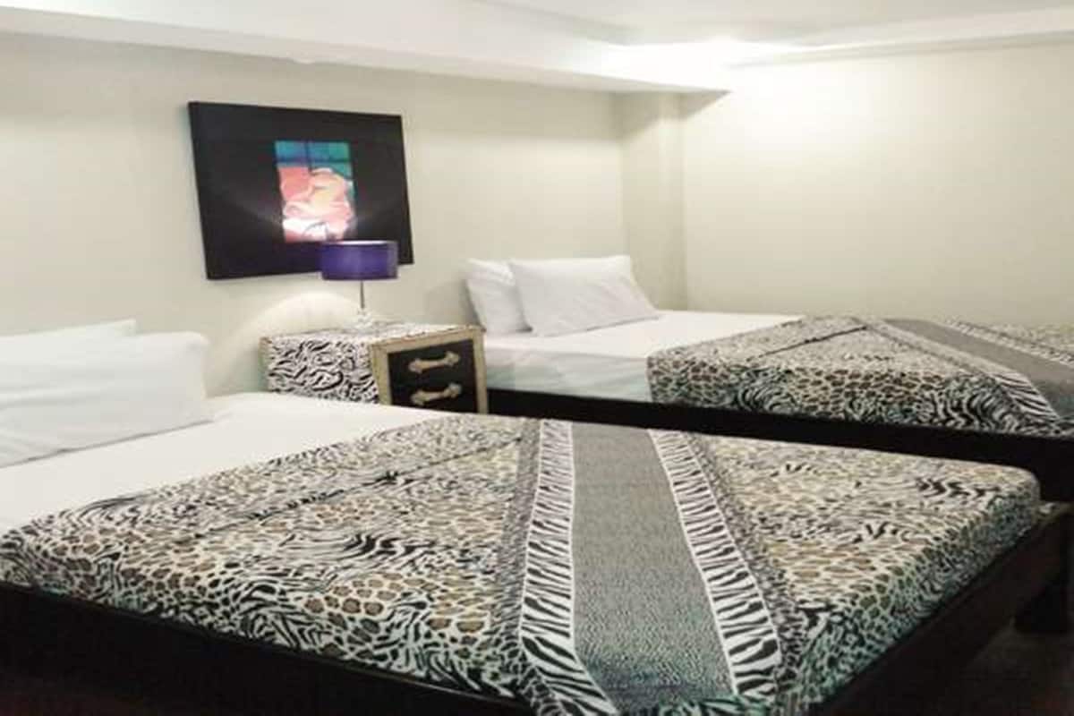 A hotel room with two beds, a nightstand, a lamp, and a wall-mounted TV.