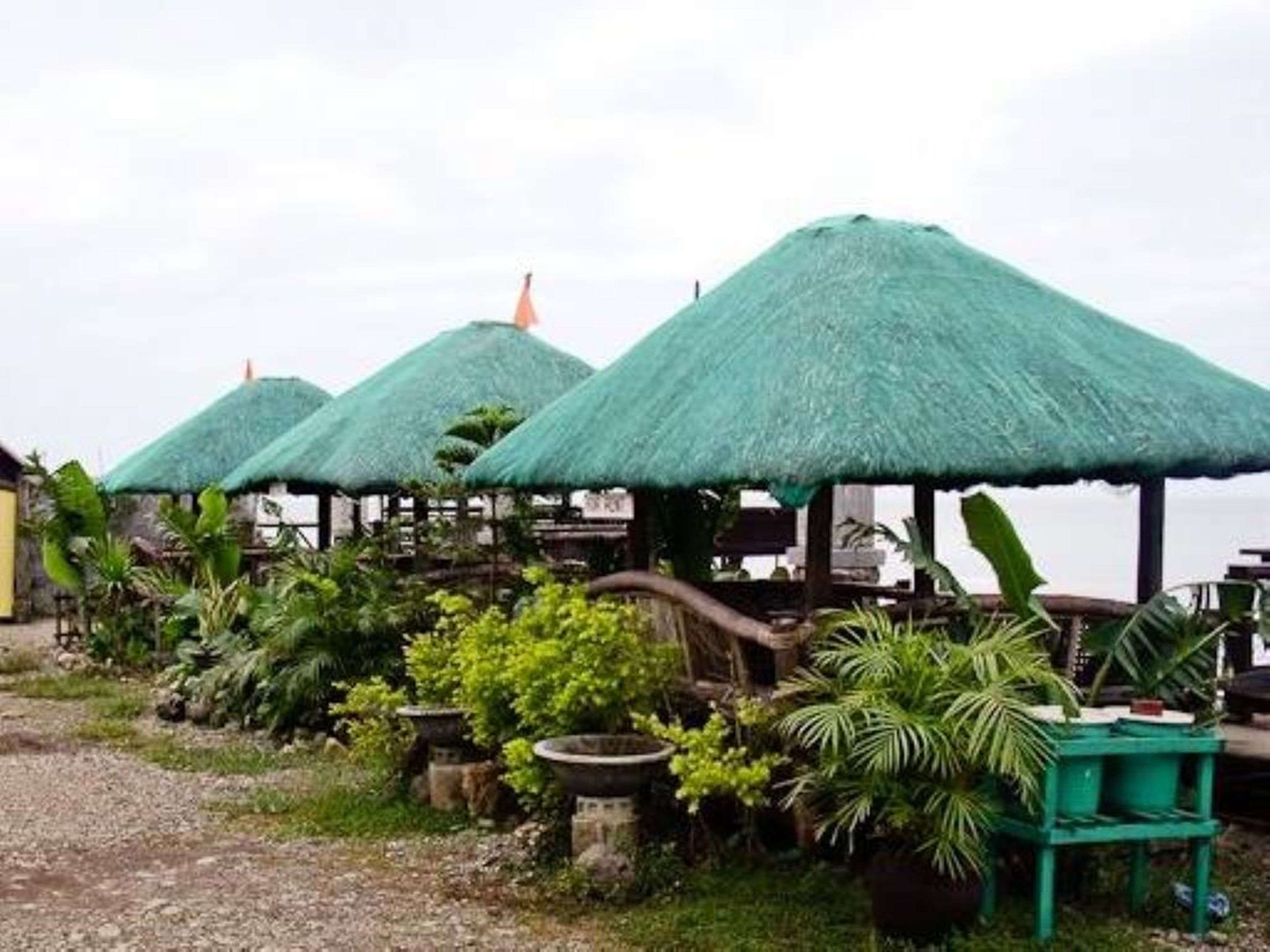 A row of thatched-roof structures with outdoor seating, surrounded by lush greenery.