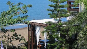 Vista a la playa con una vista despejada del mar, una pérgola de madera y un área de comedor con mesa y sillas.