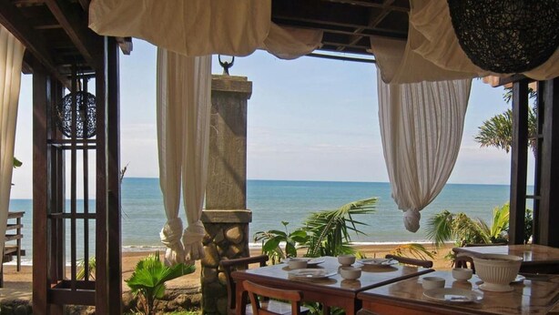 Un espacio para comer frente al mar, con vistas al océano, que incluye una mesa servida con platos y un pilar de piedra.