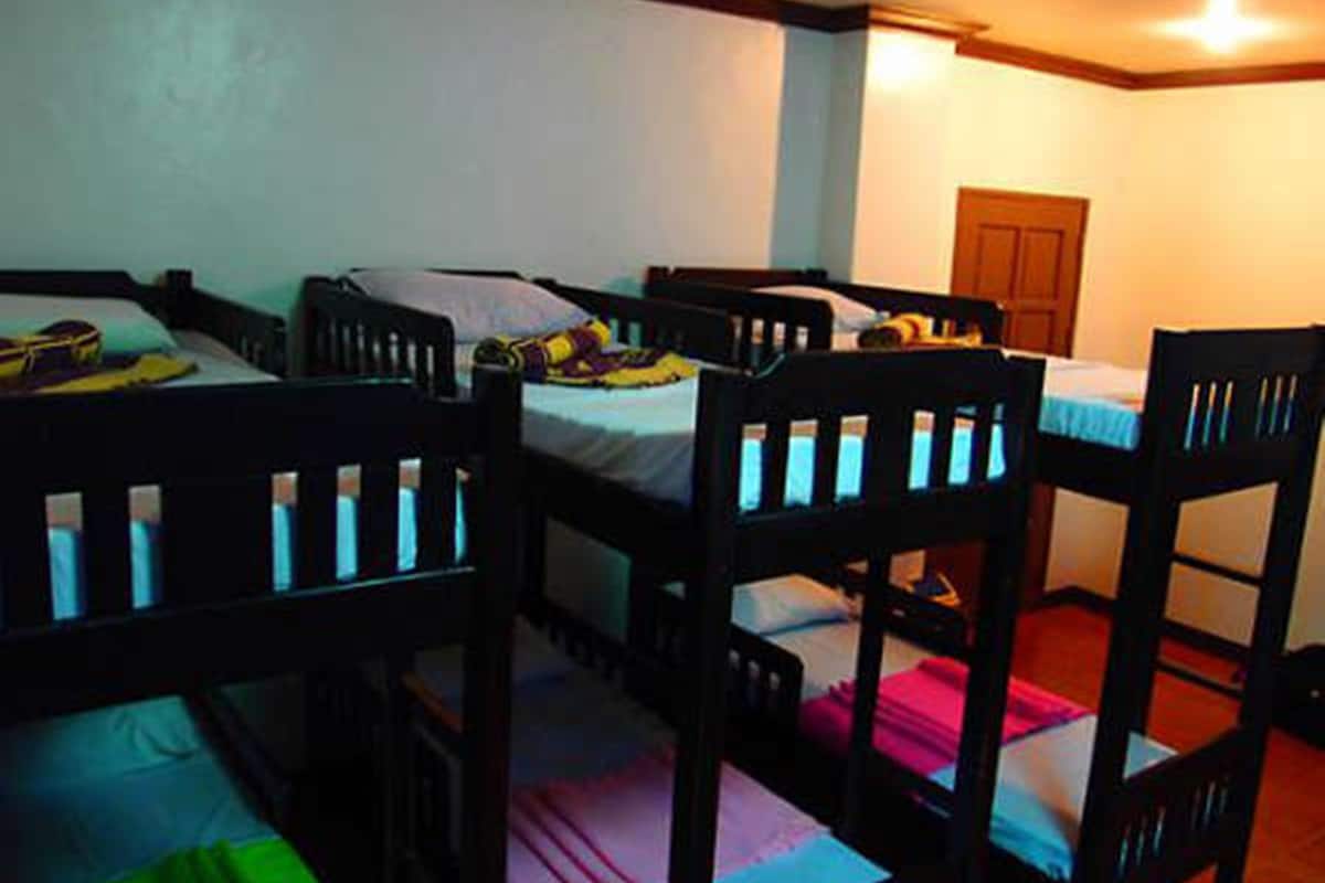 A room with four bunk beds arranged in a row, a wooden door, and a small table with a tablecloth.