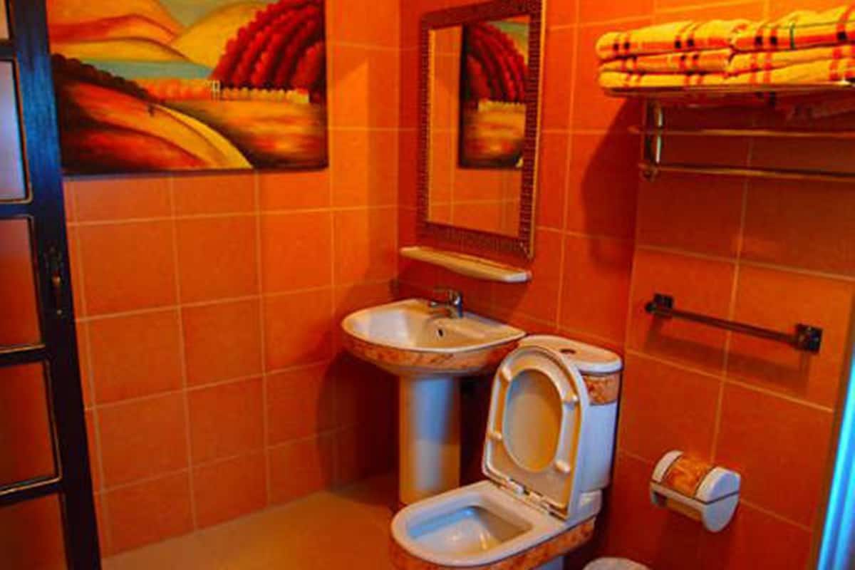 A bathroom with orange tiles, a sink, a toilet, a towel rack, and a trash bin.