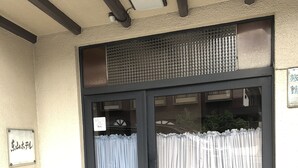 A building entrance with a dark door, two windows with curtains, and potted plants outside.