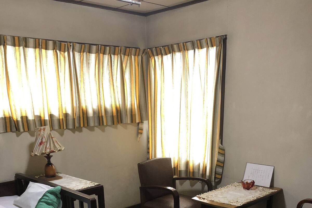 A hotel room with a bed, two chairs, a small table, a lamp, and a window with curtains.