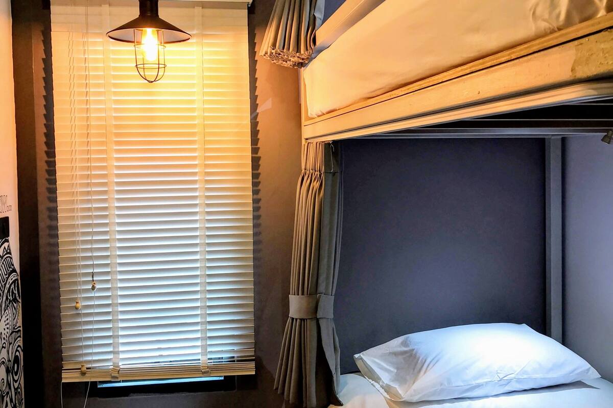 Une chambre avec un lit superposé, un bureau, un appareil de climatisation et une fenêtre avec des stores.