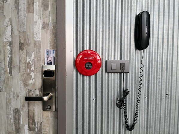 A door with a keyhole, a red fire alarm button, a telephone, and a power outlet.