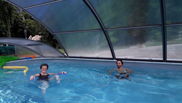 An indoor swimming pool with clear water, surrounded by a covered area with a mesh roof.