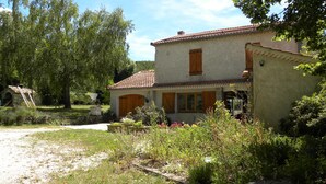 A rustic house with a tiled roof, surrounded by lush greenery and a clear sky.