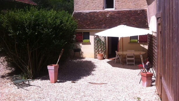 A rustic house with a gravel patio, a wooden table, and a white umbrella.