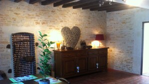 A rustic room with a brick wall, wooden table, chairs, a potted plant, a wooden cabinet, and a heart-shaped decoration.