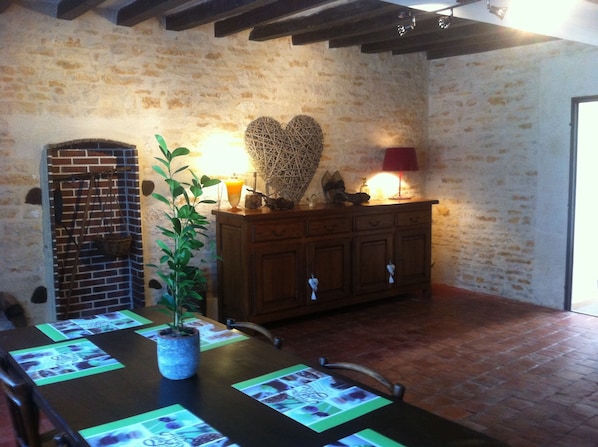A rustic room with a brick wall, wooden table, chairs, a potted plant, a wooden cabinet, and a heart-shaped decoration.