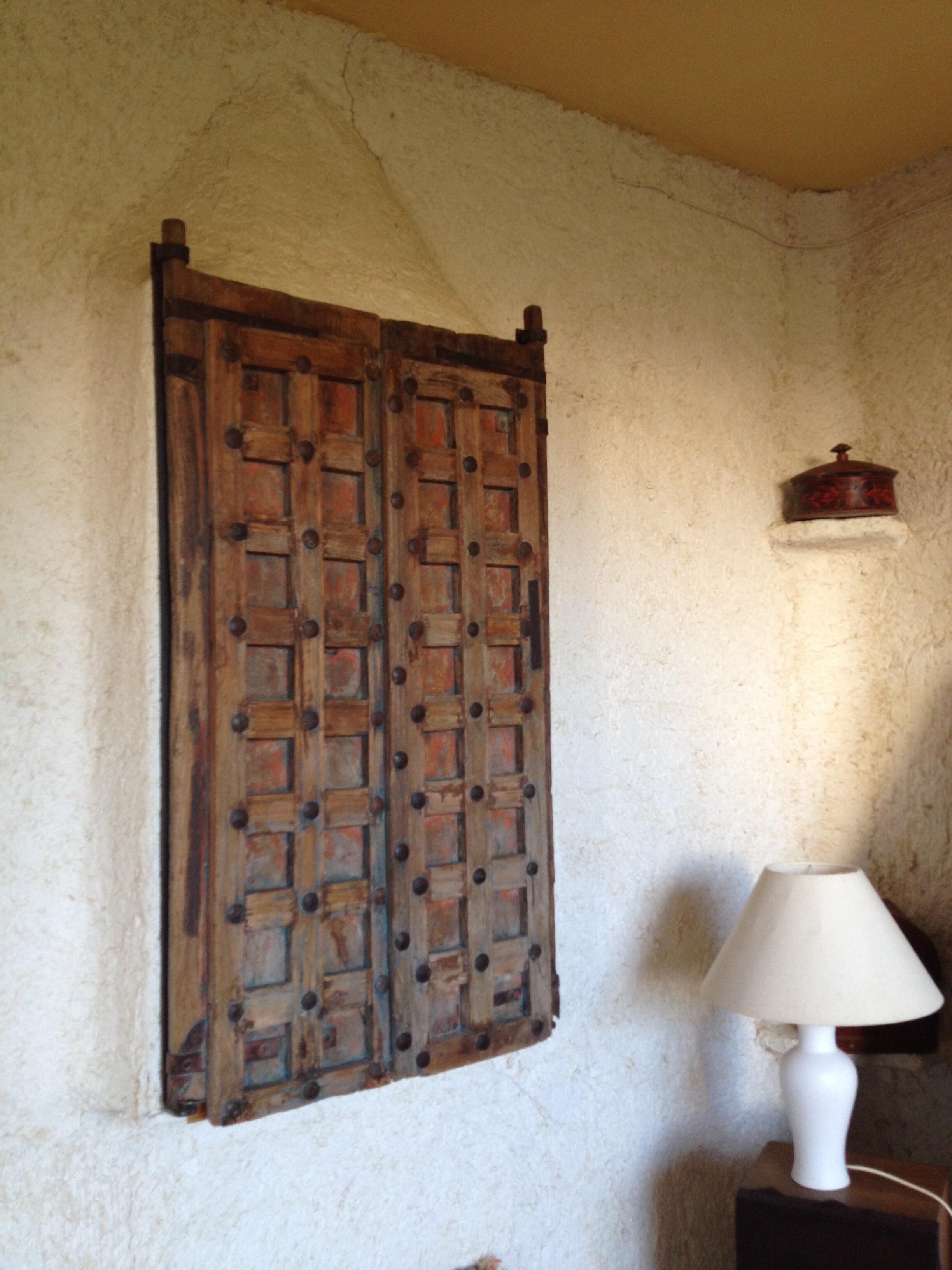 Una habitació rústica amb una porta de fusta, una làmpada blanca i una petita estant amb un recipient.