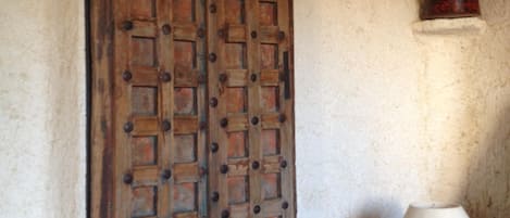 Una habitación rústica con una puerta de madera, una lámpara blanca y un pequeño estante con un recipiente.