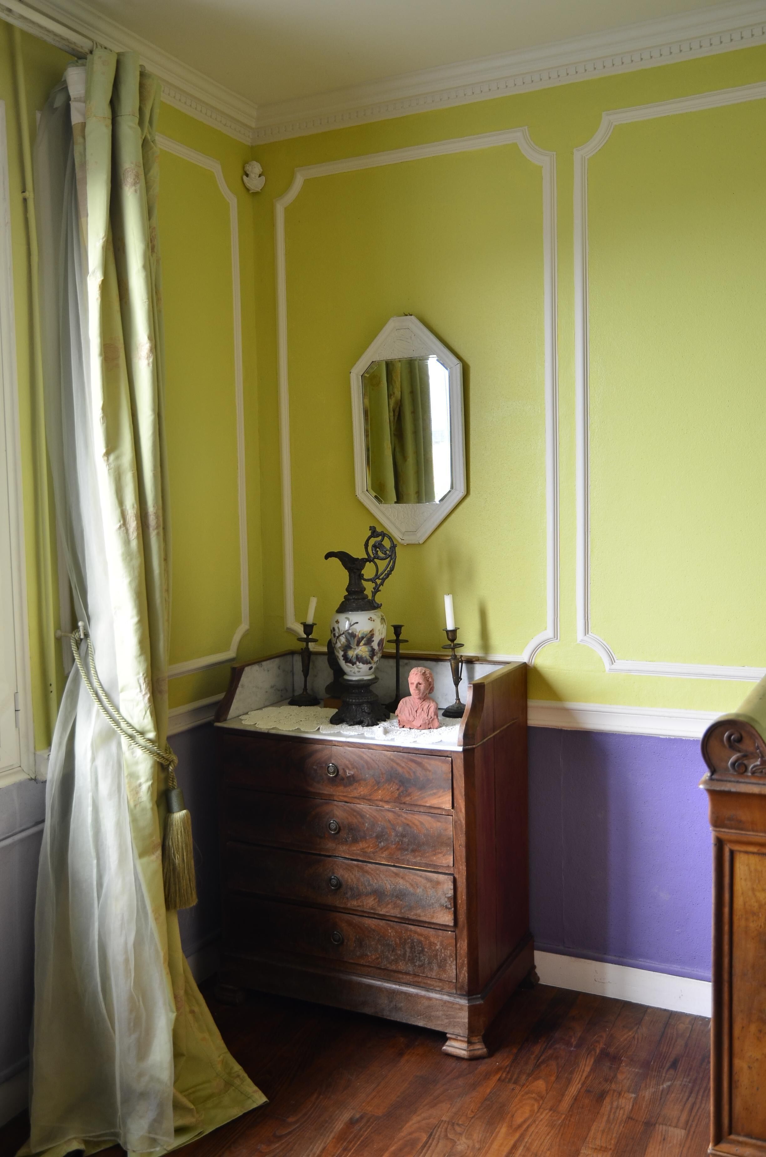 A room with a wooden dresser, a mirror, and a window with a curtain.
