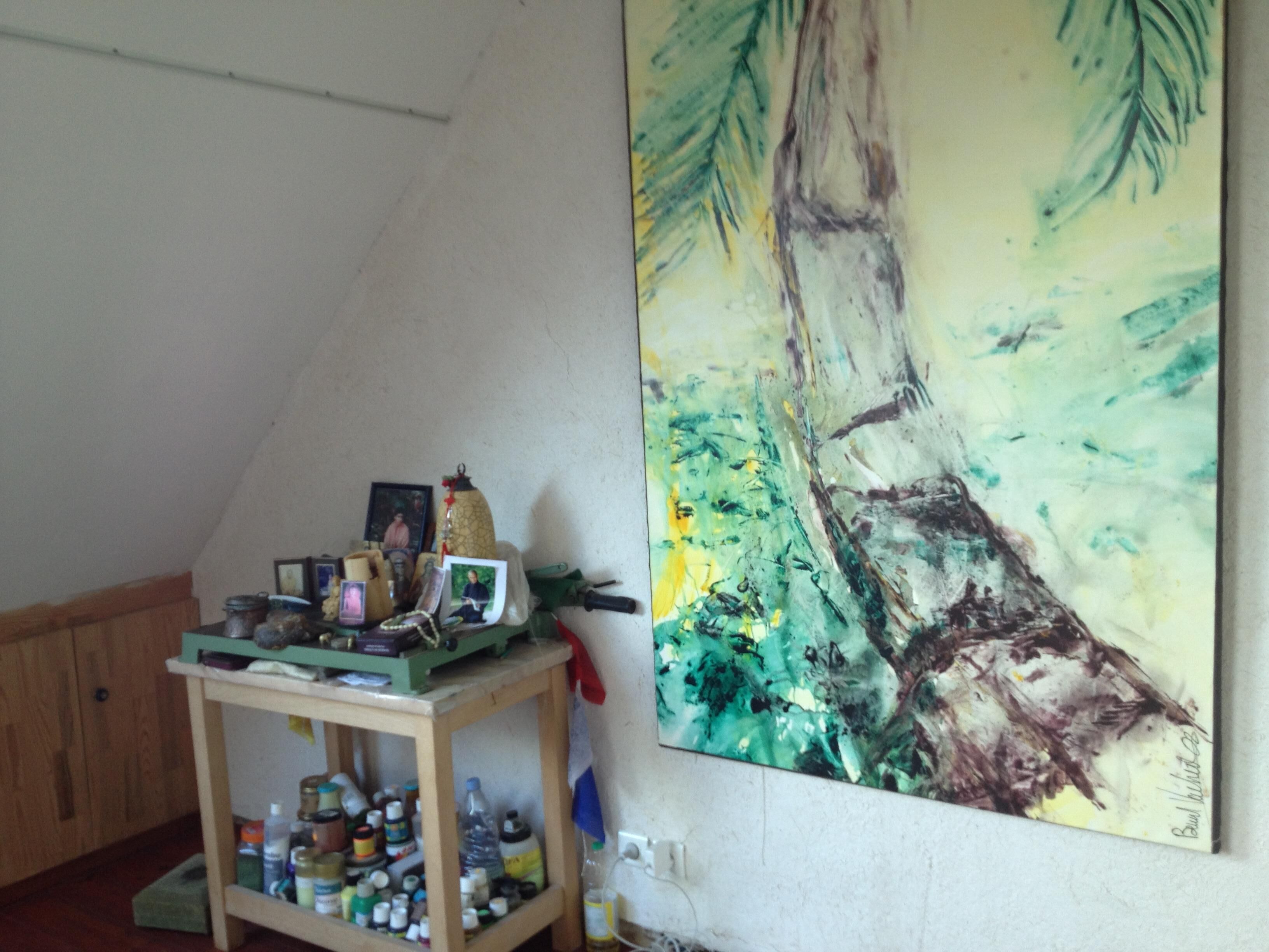 Une pièce dans laquelle on trouve un grand tableau représentant un arbre sur le mur, un meuble en bois contenant divers objets et une étagère avec des bouteilles.