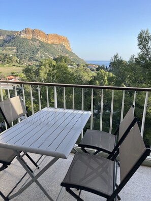 Un balcón con mesa y dos sillas, con vistas a un paisaje montañoso y al mar.