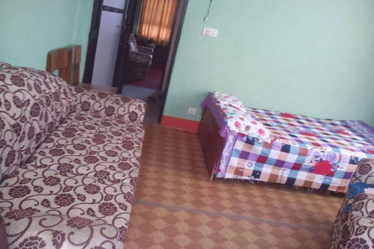 A room with a patterned sofa, a small bed with a checkered bedspread, and a tiled floor.