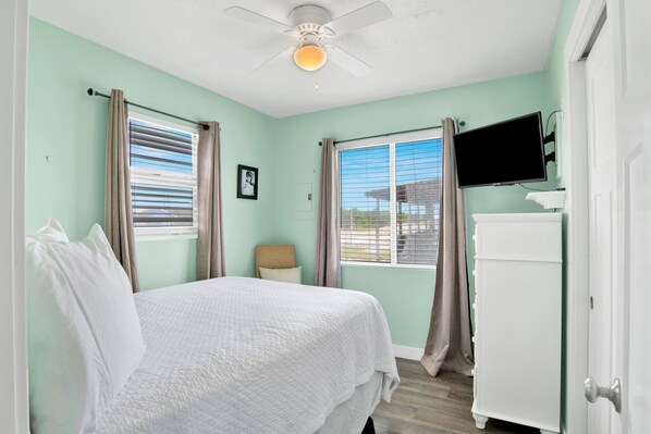 A bedroom with a bed, a ceiling fan, a TV, and a window with curtains. - Gulf Views | Pet Friendly | Steps to Beach Access (Gulf Shores)