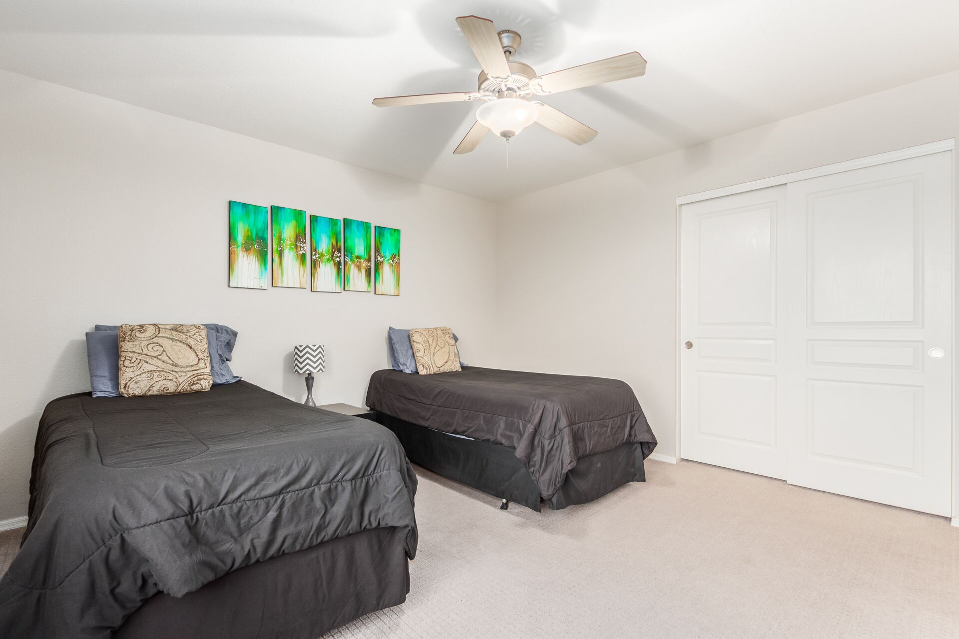 A bedroom with two beds, a ceiling fan, and a white door.