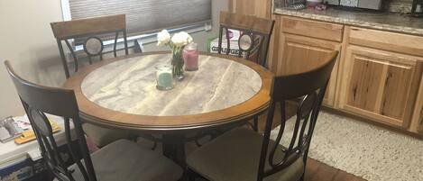 Uma área de refeições com uma mesa redonda, quatro cadeiras e um vaso com flores.