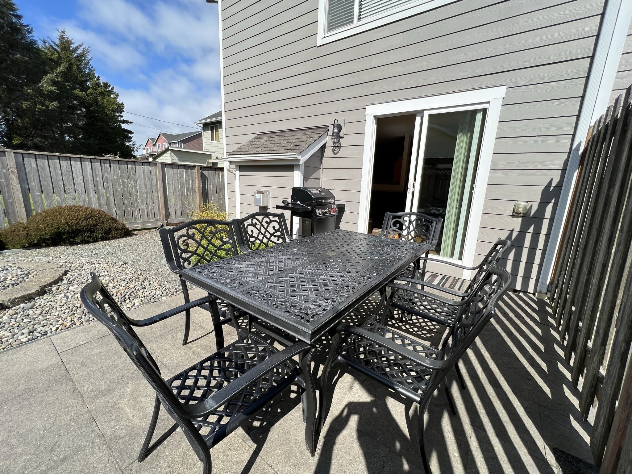 Une terrasse avec une table et des chaises en métal, un barbecue et une clôture en bois.