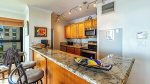 A kitchen with wooden cabinets, a granite countertop, a microwave, and a refrigerator.